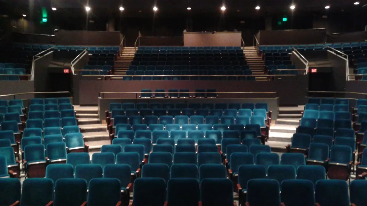 A large auditorium with blue seats and white chairs.